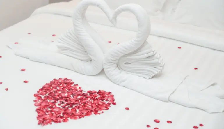 bed with white bedspread, hearts, and rose petals
